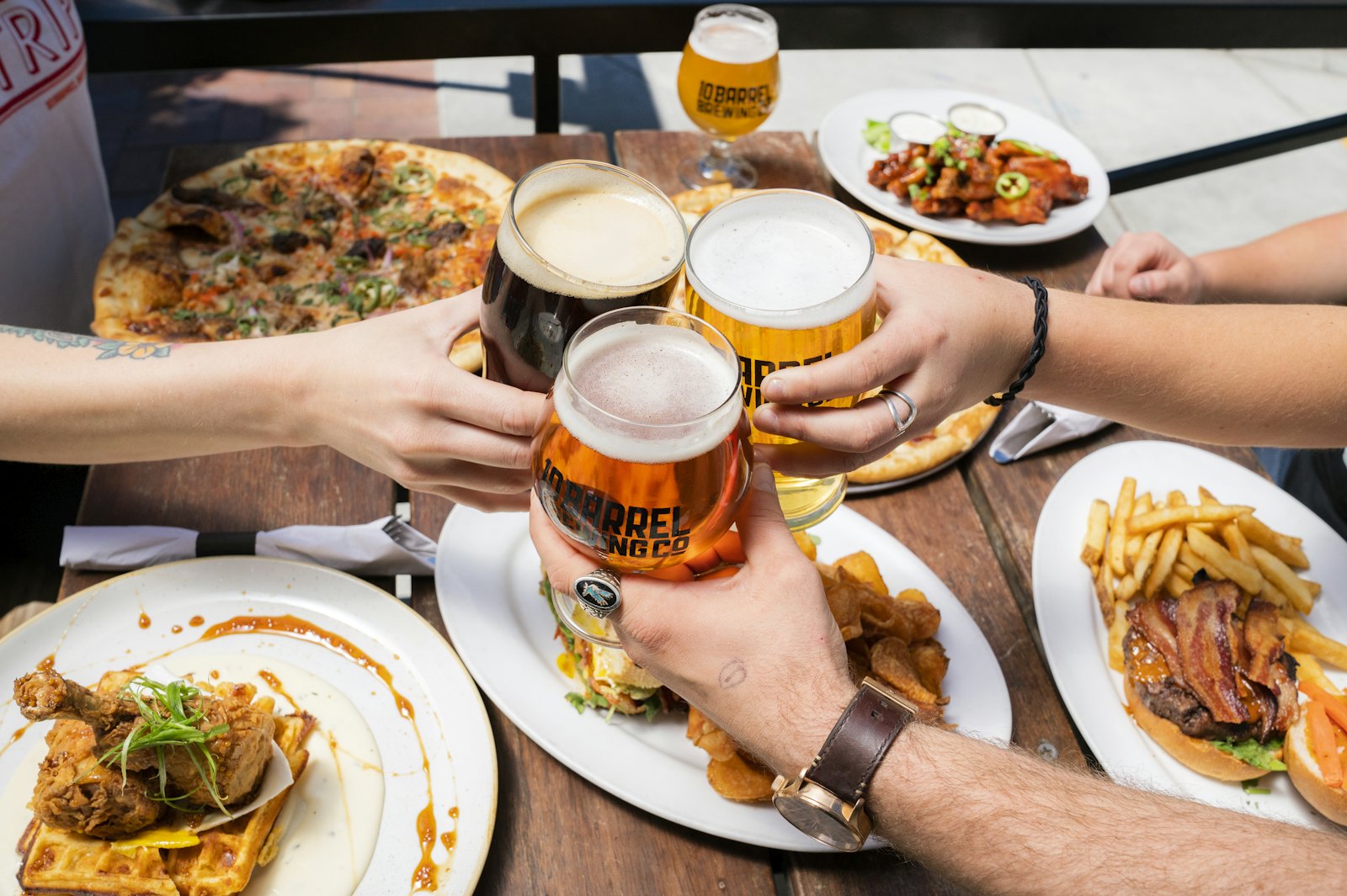 Anstoßen mit Bier, auf dem Tisch Pizza und Pommes