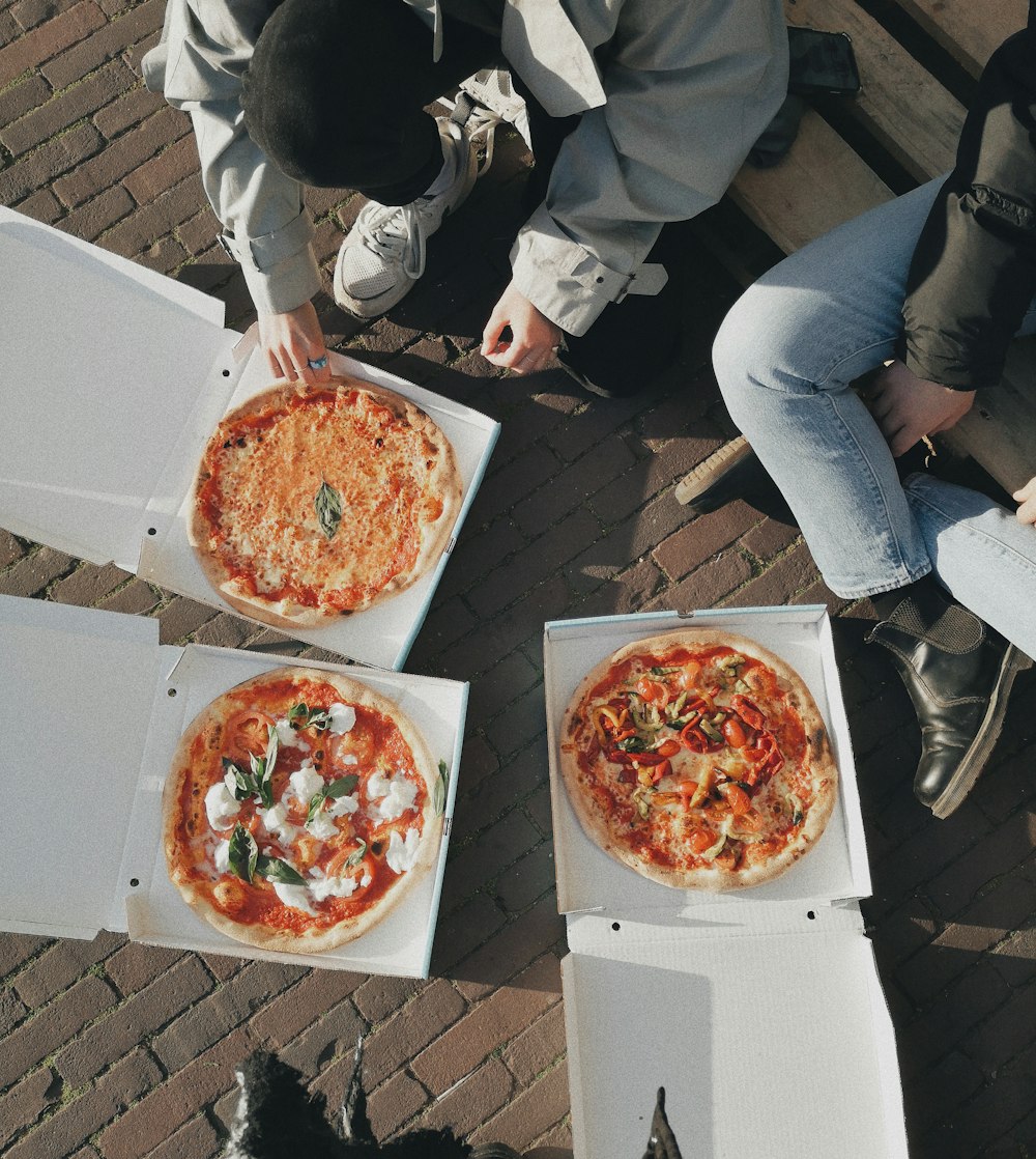 Drei Pizzen in offenen Kartons, draußen auf einer Bank